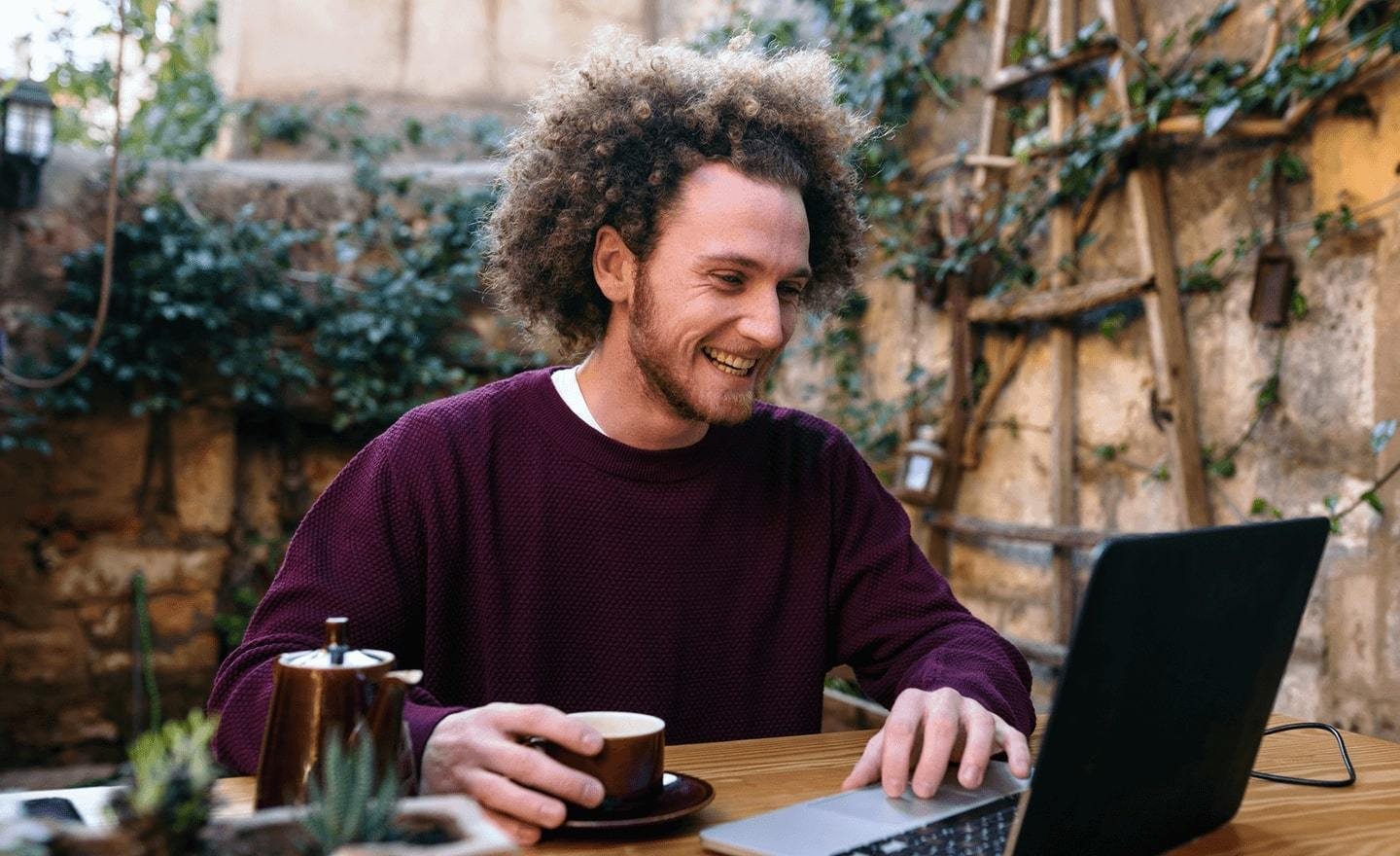 Man sitting at table drinking coffee and looking at laptop