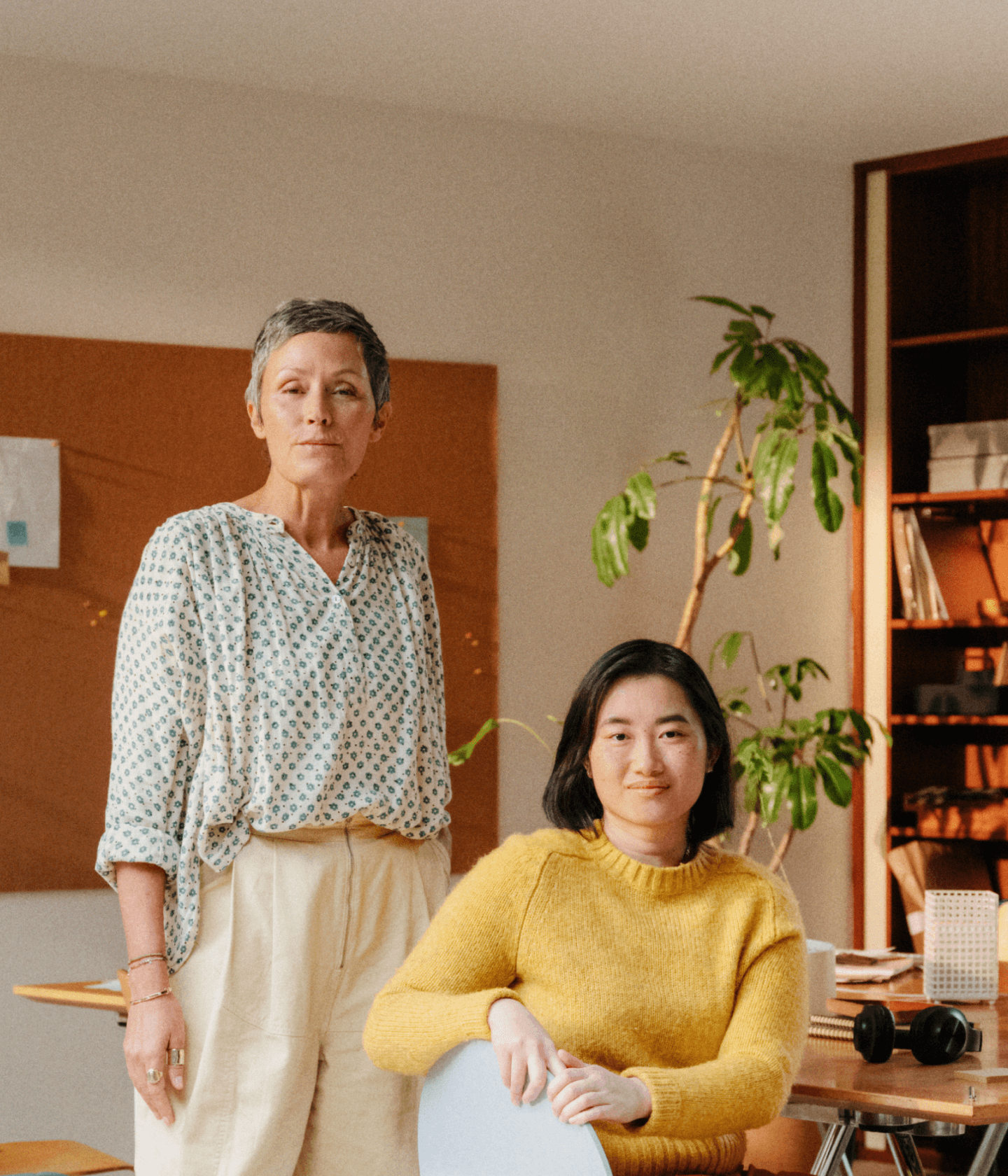 Two women in a warm and colorful toned office facing camera