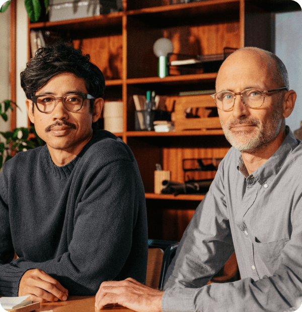 Two men sitting in an office space with warm tones2x