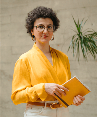 Woman posing in yellow blouse holding a notebook